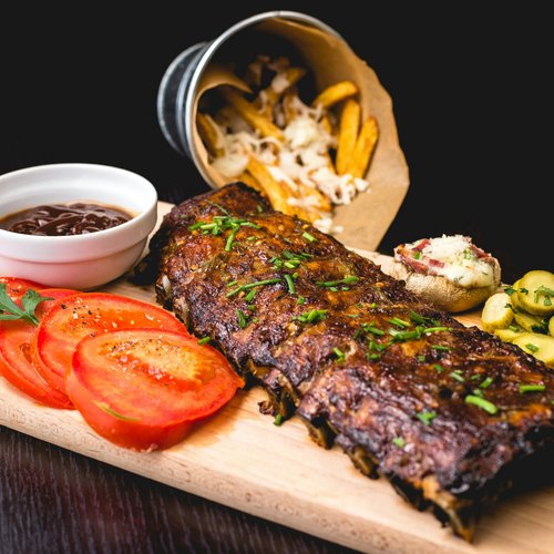Pure Flexibilität im TYROL Family Retreat Gegrillte Rippchen mit Tomatenscheiben, Dip, Pommes und Beilagen auf Holzbrett