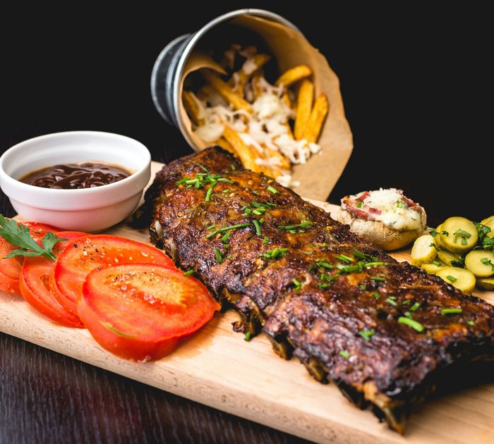 Pure Flexibilität im TYROL Family Retreat Gegrillte Rippchen mit Tomatenscheiben, Dip, Pommes und Beilagen auf Holzbrett