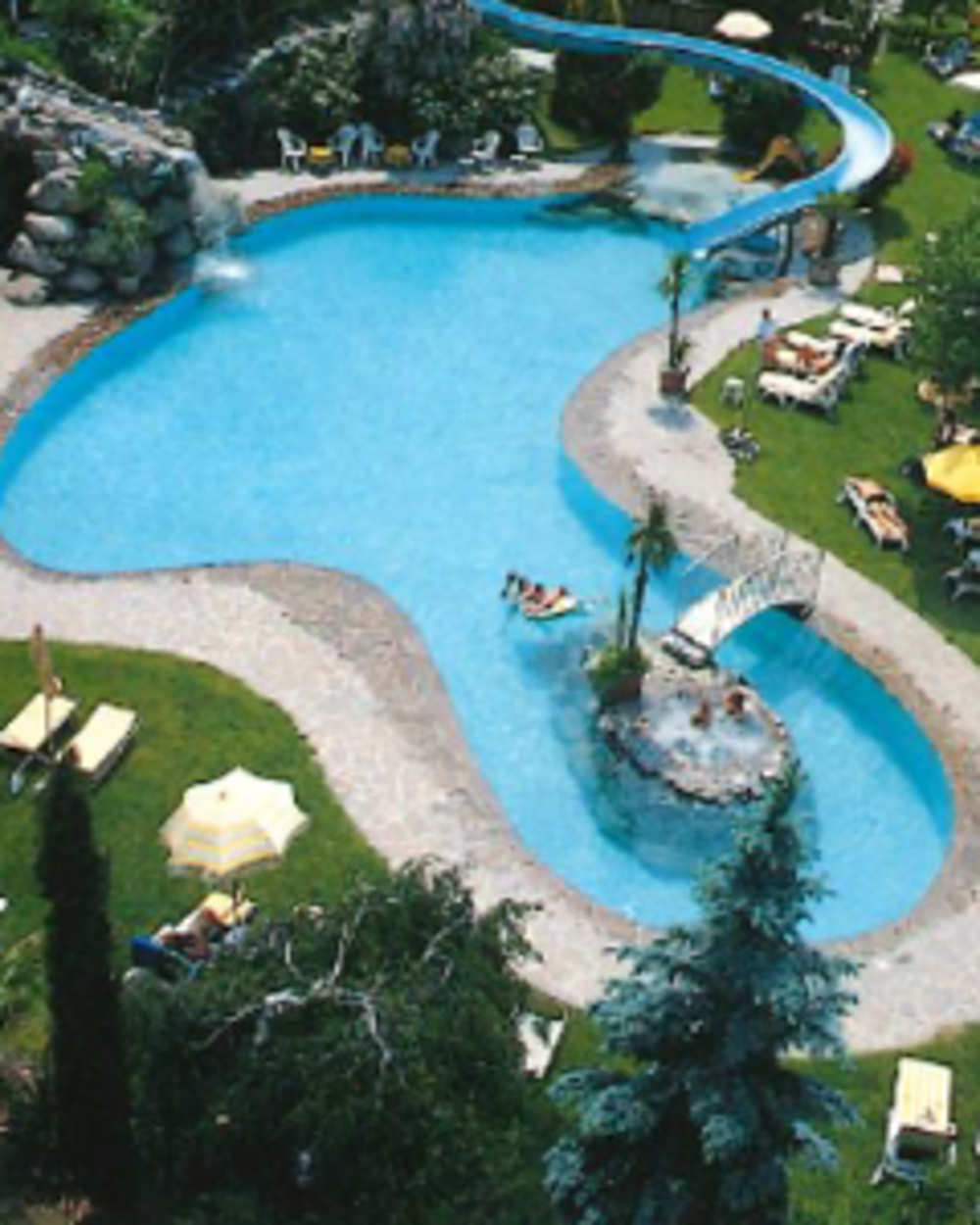 Eure Märchenwelt: das 4-Sterne-Hotel in Naturns Außenpool mit Rutsche und Liegestühlen in grüner Gartenanlage