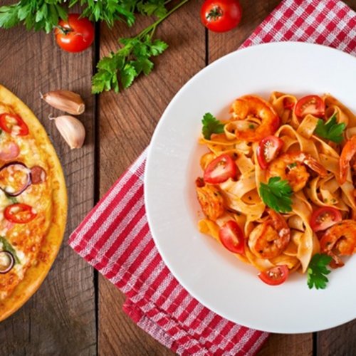Pure Flexibilität im TYROL Family Retreat Pizza und Garnelen-Pasta auf Holztisch mit roten und grünen Zutaten