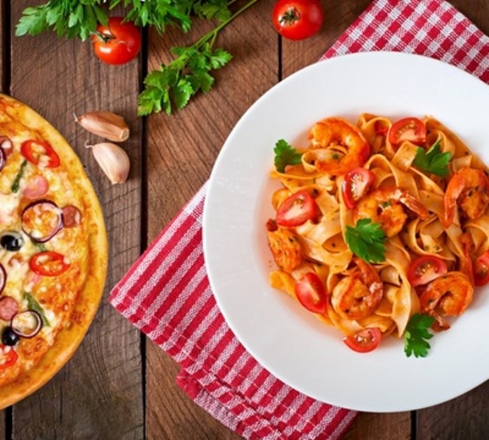 Pure Flexibilität im TYROL Family Retreat Pizza und Garnelen-Pasta auf Holztisch mit roten und grünen Zutaten