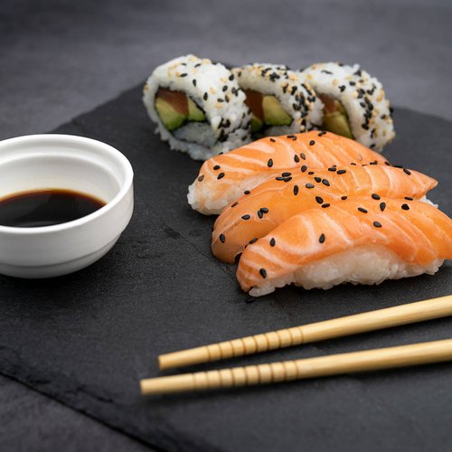 Pure Flexibilität im TYROL Family Retreat Sushi mit Lachs, California Rolls, Sojasauce und Essstäbchen auf schwarzem Stein