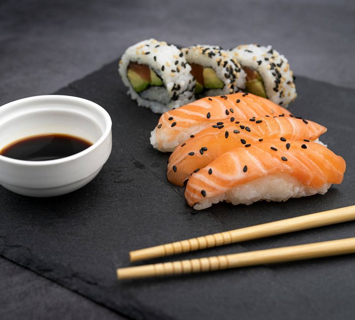 Pure Flexibilität im TYROL Family Retreat Sushi mit Lachs, California Rolls, Sojasauce und Essstäbchen auf schwarzem Stein
