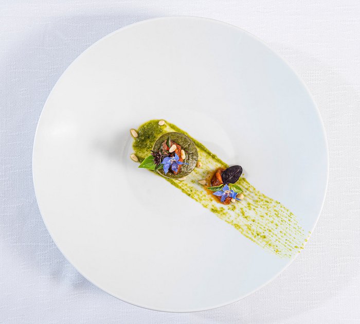 Pure Flexibilität im TYROL Family Retreat Kunstvoll angerichtetes Gericht mit grüner Sauce, Kräutern und essbaren Blumen auf weißem Teller