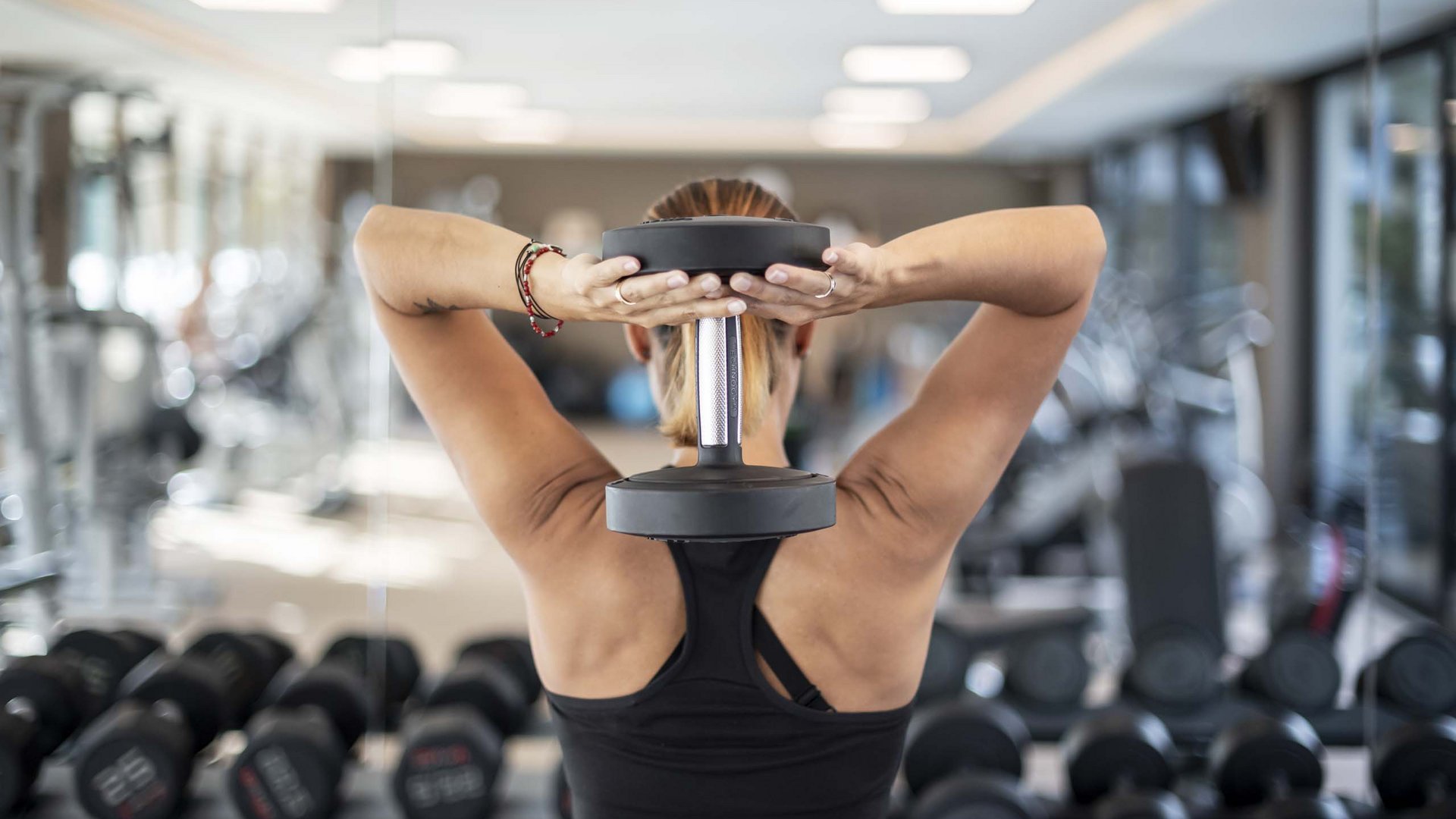 Workout im Hotel mit Fitnessstudio in Südtirol Frau hebt Kurzhantel hinter dem Kopf im Fitnessstudio