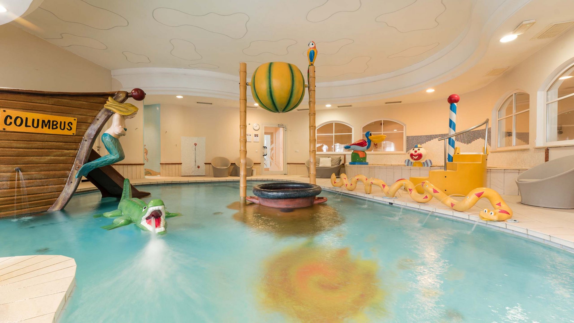 TYROL Family Retreat als Familienhotels in Südtirol Innenkinderpool mit Bootsrutsche und Wasserspielzeug in gelbem Raum