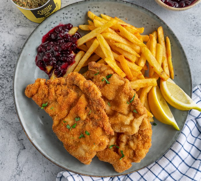 Pure Flexibilität im TYROL Family Retreat Schnitzel mit Pommes, Zitronenspalten und Preiselbeersauce auf einem Teller