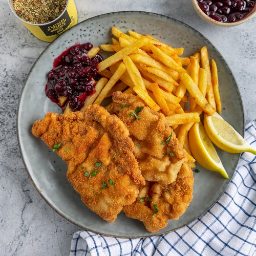Pure Flexibilität im TYROL Family Retreat Schnitzel mit Pommes, Zitronenspalten und Preiselbeersauce auf einem Teller
