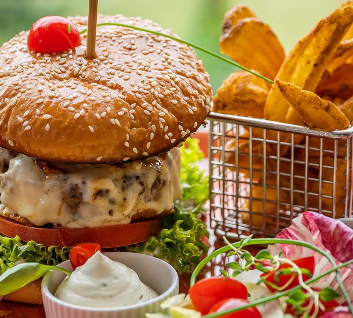 Pure Flexibilität im TYROL Family Retreat Hamburger mit Käse, Salat, Pommes und Dips auf einem Teller