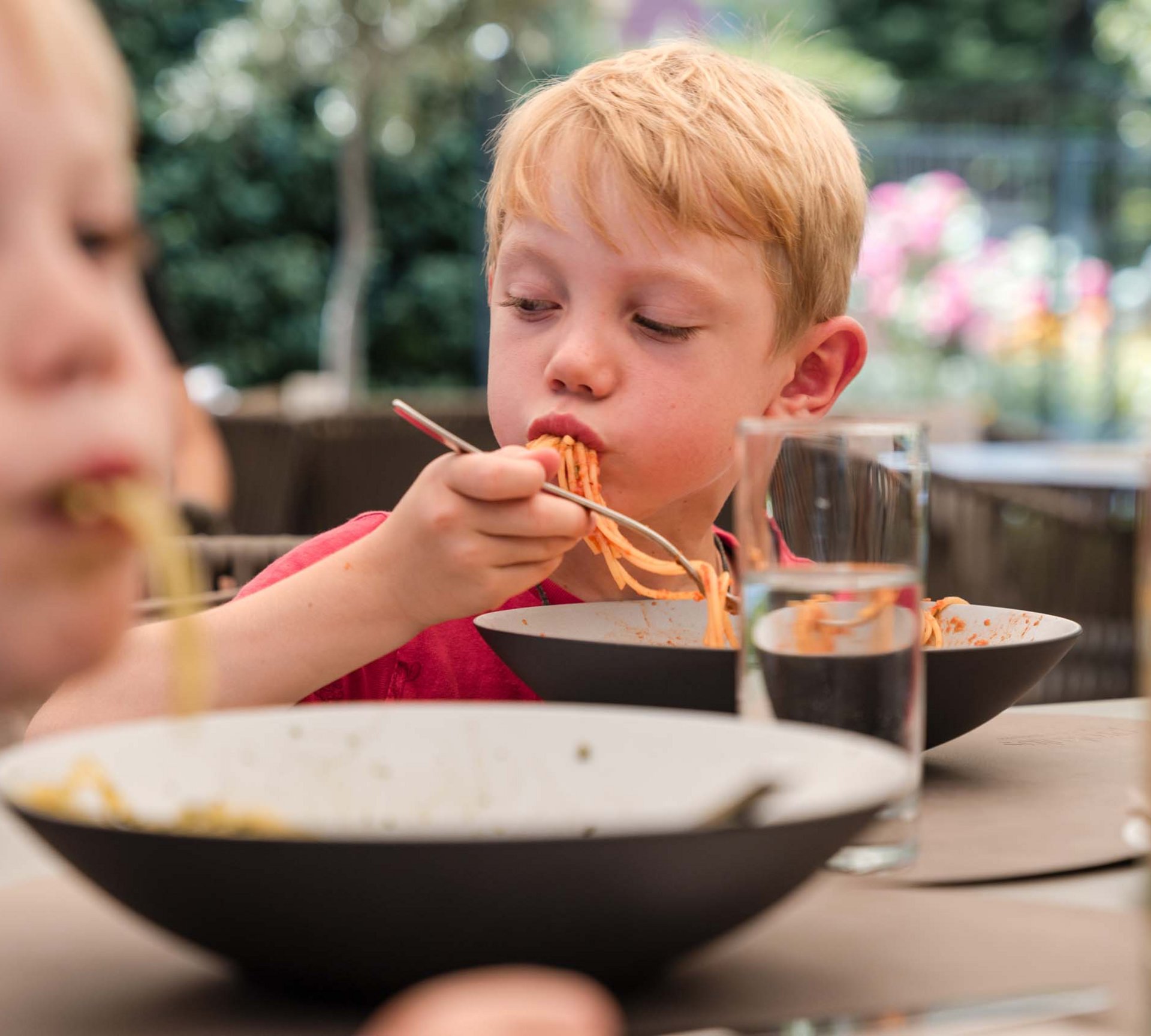 Pure Flexibilität im TYROL Family Retreat Zwei Jungen essen Spaghetti am Tisch im Freien