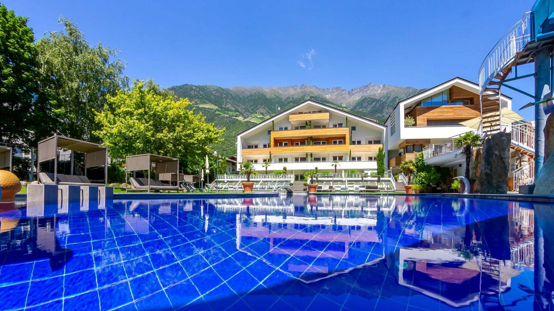 TYROL Family Retreat als Familienhotels in Südtirol Pool mit blauem Wasser vor modernem Hotelgebäude in den Bergen