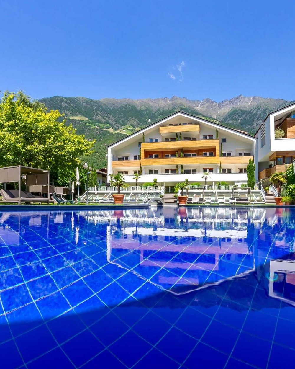 Eure Märchenwelt: das 4-Sterne-Hotel in Naturns Pool mit blauem Wasser vor modernem Hotelgebäude in den Bergen