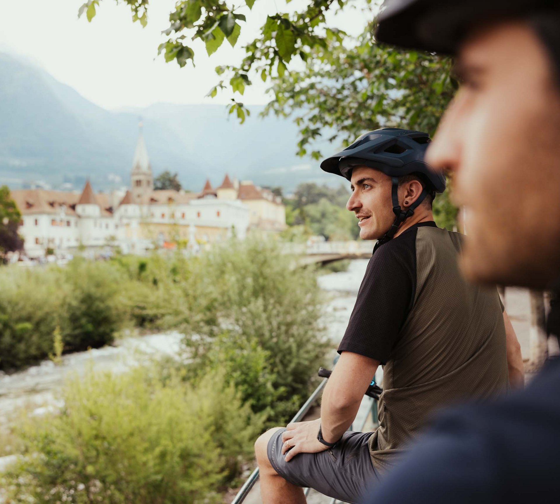 Euer E-Bike-Hotel in Südtirol Zwei Radfahrer mit Helmen genießen Aussicht auf Fluss und historische Stadt