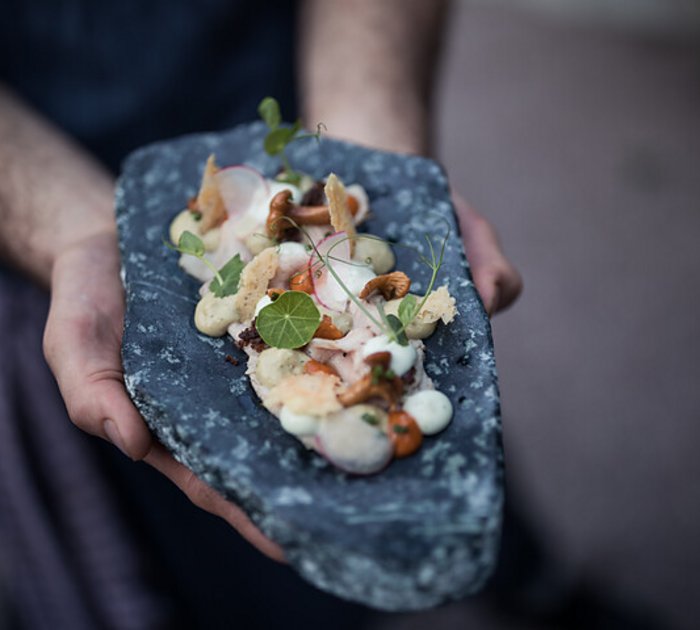Pure Flexibilität im TYROL Family Retreat Person hält kunstvoll angerichtete Gourmet-Garnitur auf einem Stein-Servierteller