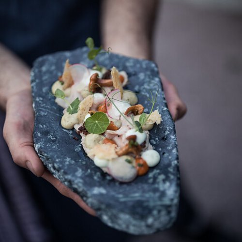 Pure Flexibilität im TYROL Family Retreat Person hält kunstvoll angerichtete Gourmet-Garnitur auf einem Stein-Servierteller
