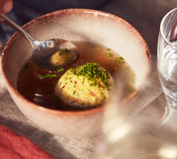 Pure Flexibilität im TYROL Family Retreat Schale mit Bouillon und Semmelknödel, daneben ein Glas Wasser