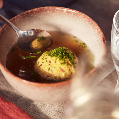 Pure Flexibilität im TYROL Family Retreat Schale mit Bouillon und Semmelknödel, daneben ein Glas Wasser