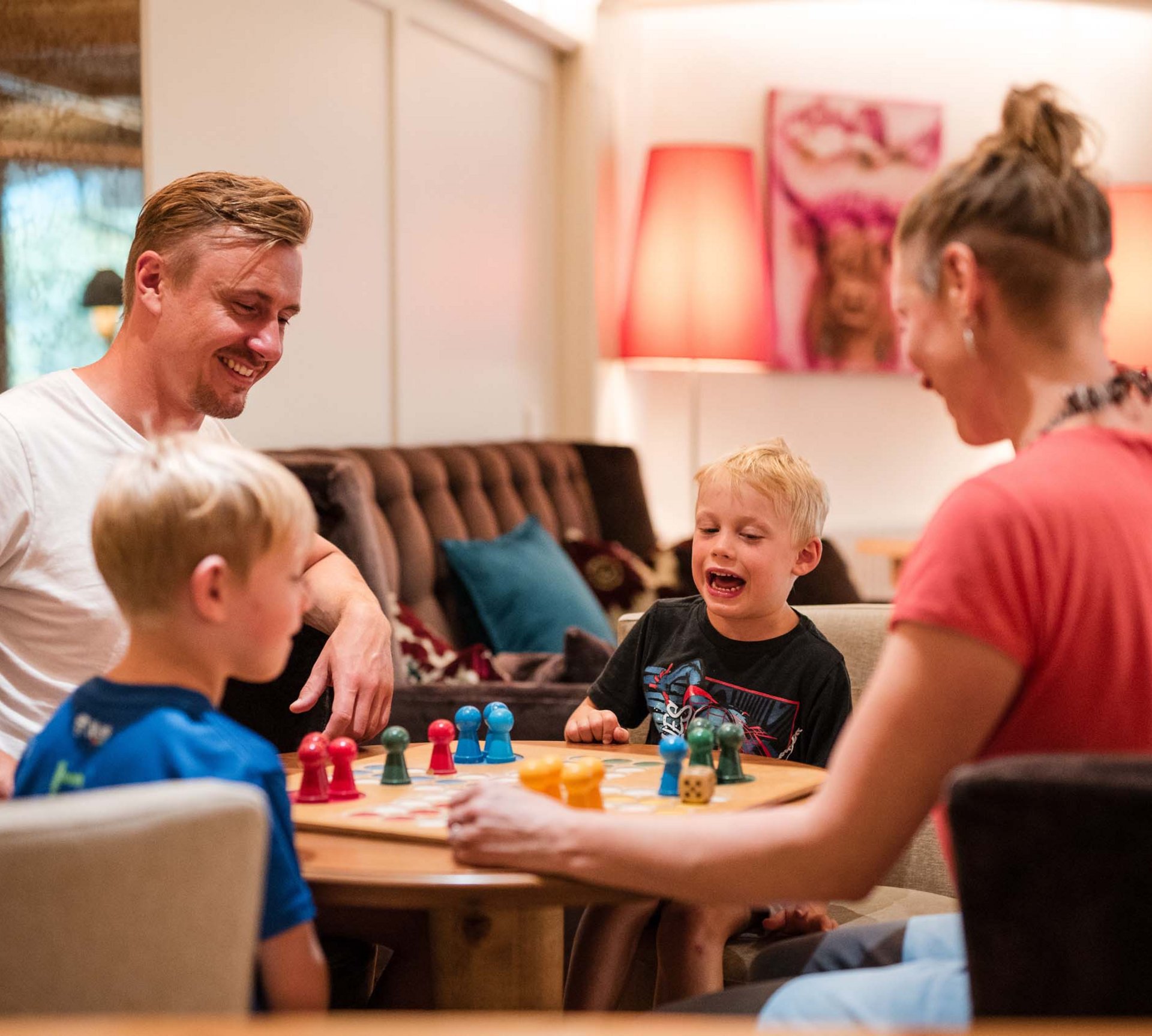 Spiel und Spaß im Hotel mit Kinderbetreuung in Südtirol Familie spielt Brettspiel gemeinsam am Tisch im Wohnzimmer