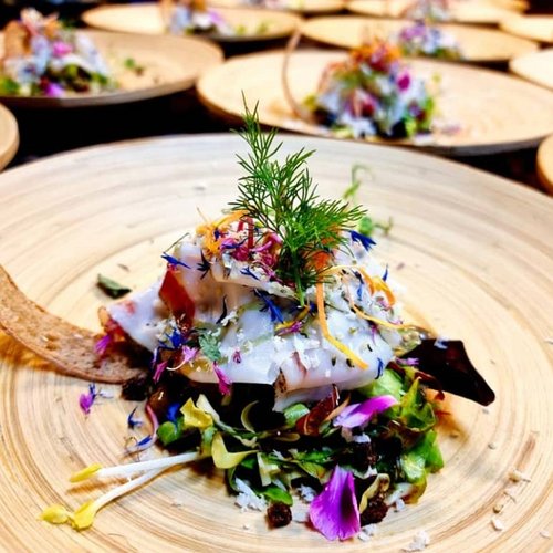 Pure Flexibilität im TYROL Family Retreat Fein angerichteter Salat mit essbaren Blüten auf einem Holzteller