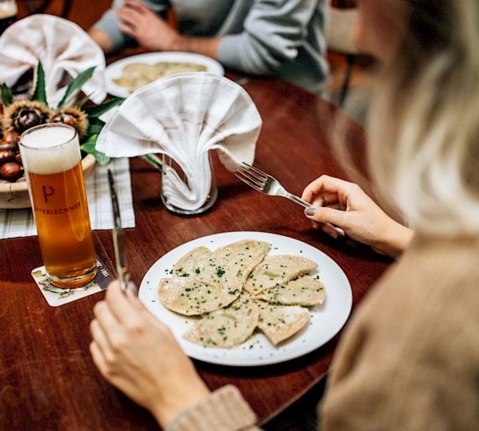 Pure Flexibilität im TYROL Family Retreat Frau isst Ravioli mit Bier an einem gedeckten Holztisch.