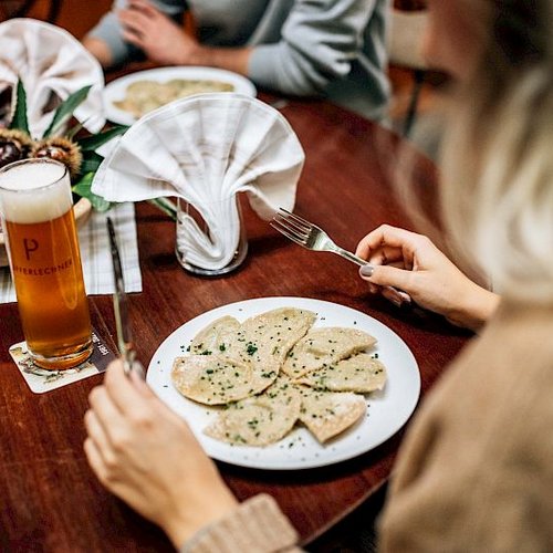 Pure Flexibilität im TYROL Family Retreat Frau isst Ravioli mit Bier an einem gedeckten Holztisch.