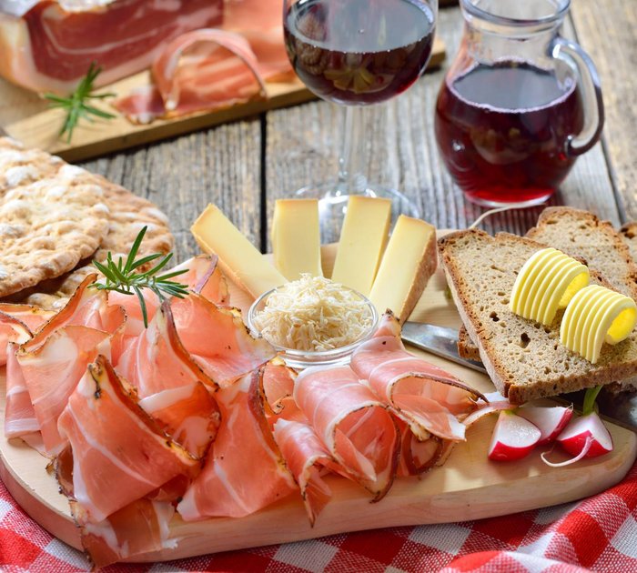 Pure Flexibilität im TYROL Family Retreat Brett mit Speck, Käse, Brot, Butter, Brotchips und Rotwein auf Holztisch