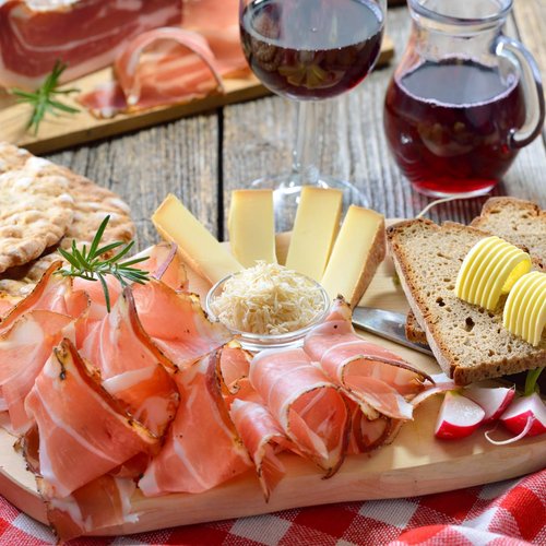 Pure Flexibilität im TYROL Family Retreat Brett mit Speck, Käse, Brot, Butter, Brotchips und Rotwein auf Holztisch