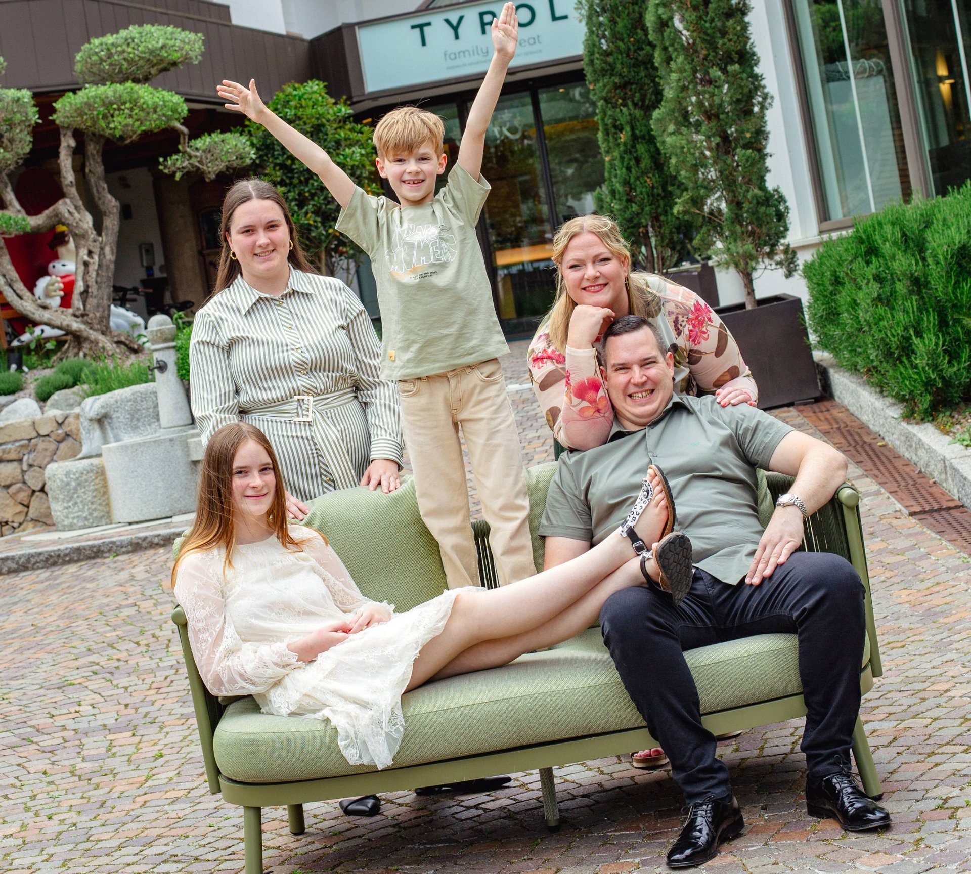 Eure Märchenwelt: das 4-Sterne-Hotel in Naturns Fröhliche Familie mit zwei Kindern vor Tyrol Familienhotel auf grünem Sofa
