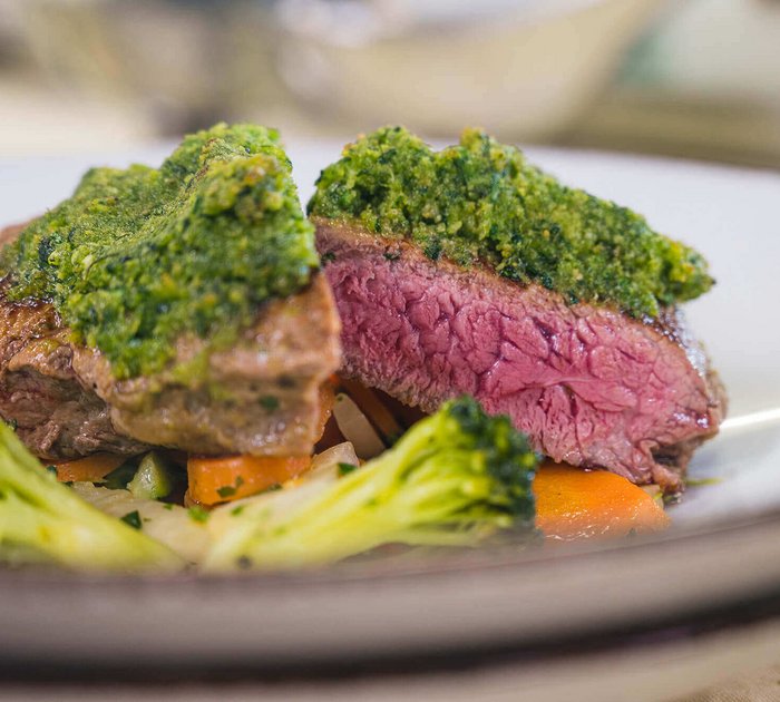 Pure Flexibilität im TYROL Family Retreat Saftiges Steak mit grüner Kräuterkruste und Gemüse auf weißem Teller