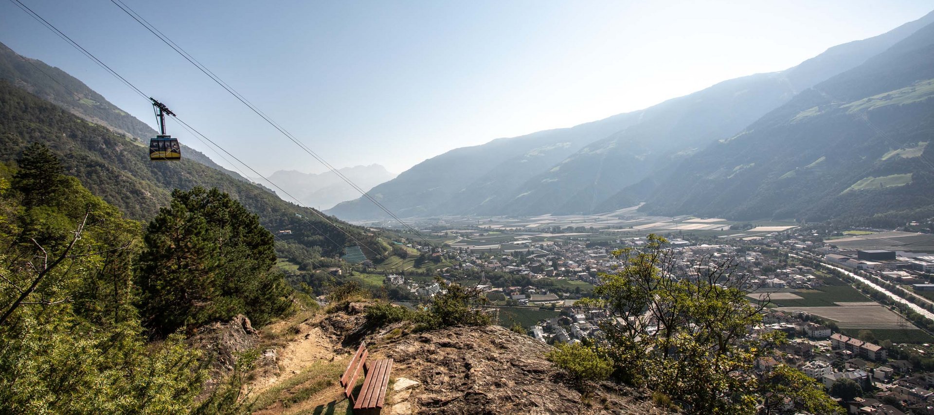 Langeweile ade im Aktivhotel in Südtirol Bank auf Felsen mit Blick auf Tal und Seilbahn in den Bergen