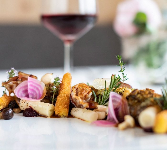 Pure Flexibilität im TYROL Family Retreat Gourmet-Gemüseplatte mit frischen Kräutern und Rotwein im Hintergrund