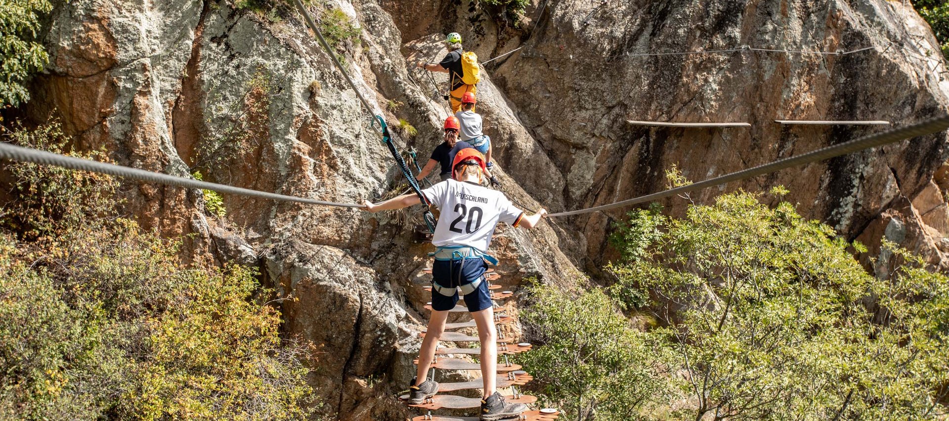 Langeweile ade im Aktivhotel in Südtirol Kinder klettern gesichert über eine Hängebrücke an einer Felswand