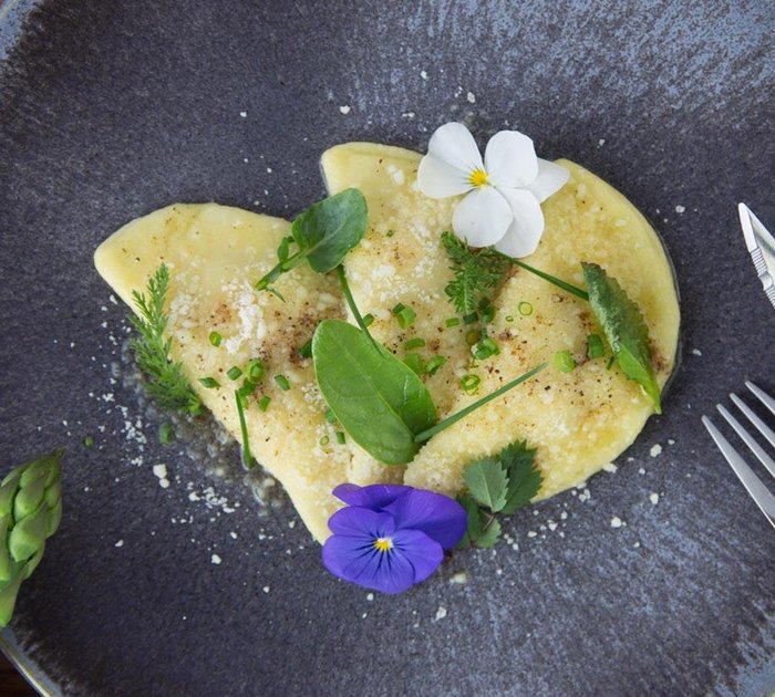Pure Flexibilität im TYROL Family Retreat Ravioli mit Kräutern und essbaren Blüten auf blauem Teller mit Besteck