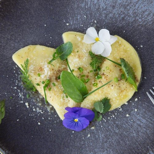 Pure Flexibilität im TYROL Family Retreat Ravioli mit Kräutern und essbaren Blüten auf blauem Teller mit Besteck