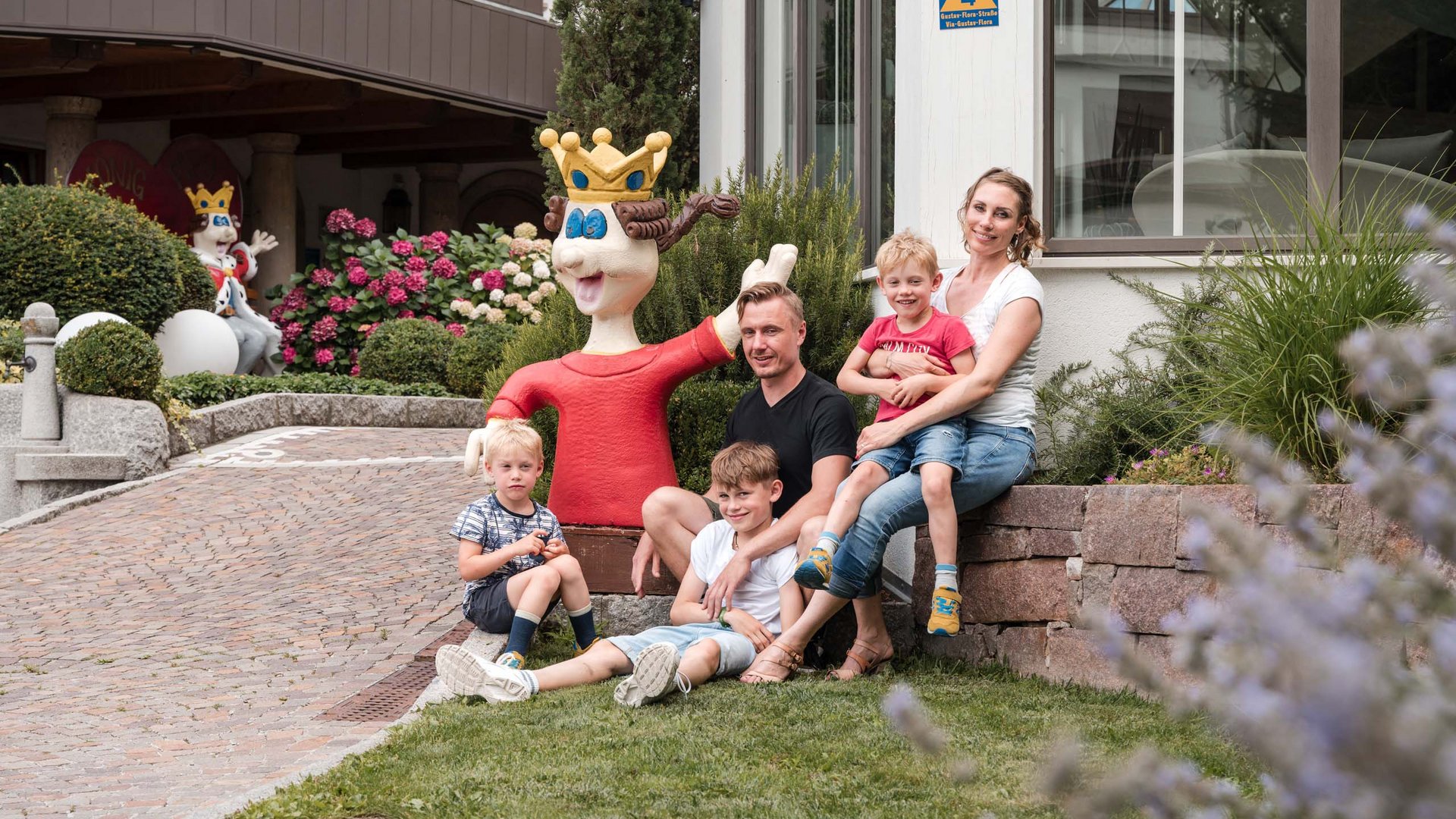 TYROL Family Retreat als Familienhotels in Südtirol Familie mit drei Kindern sitzt im Garten neben einer bunten König-Figur