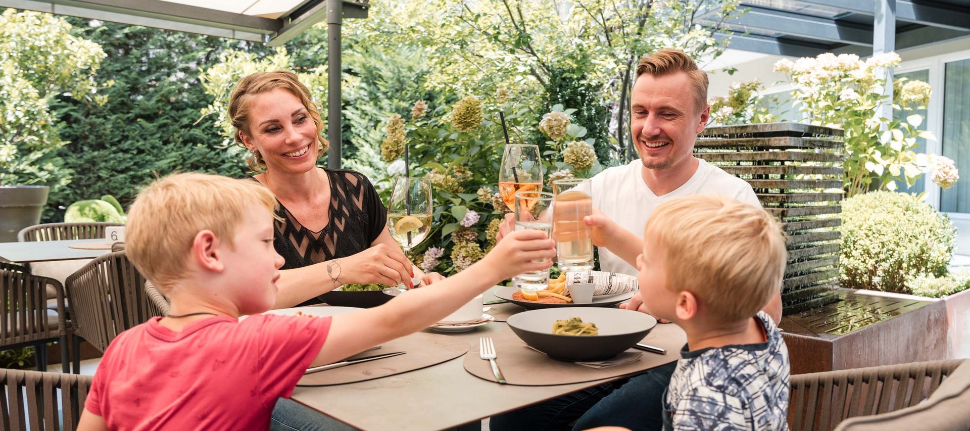 Pure Flexibilität im TYROL Family Retreat Familie beim gemeinsamen Anstoßen beim Essen im Garten