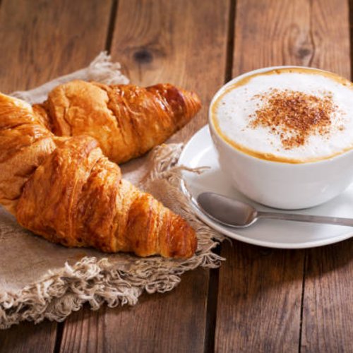 Pure Flexibilität im TYROL Family Retreat Zwei Croissants auf einem Tuch neben einer Tasse Cappuccino auf Holztisch