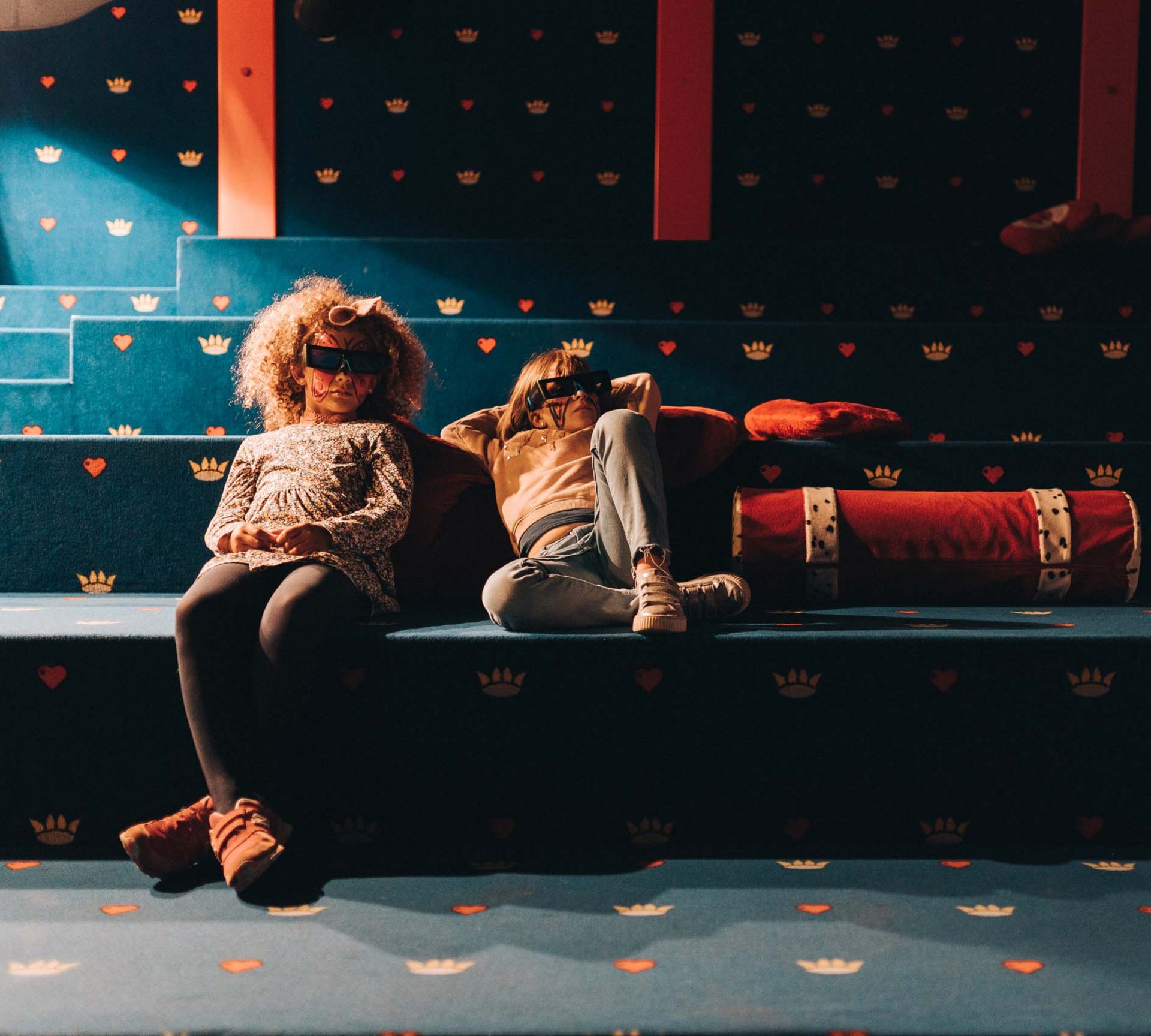 Spiel und Spaß im Hotel mit Kinderbetreuung in Südtirol Zwei Kinder mit 3D-Brillen sitzen auf bunter Treppe mit Kissen