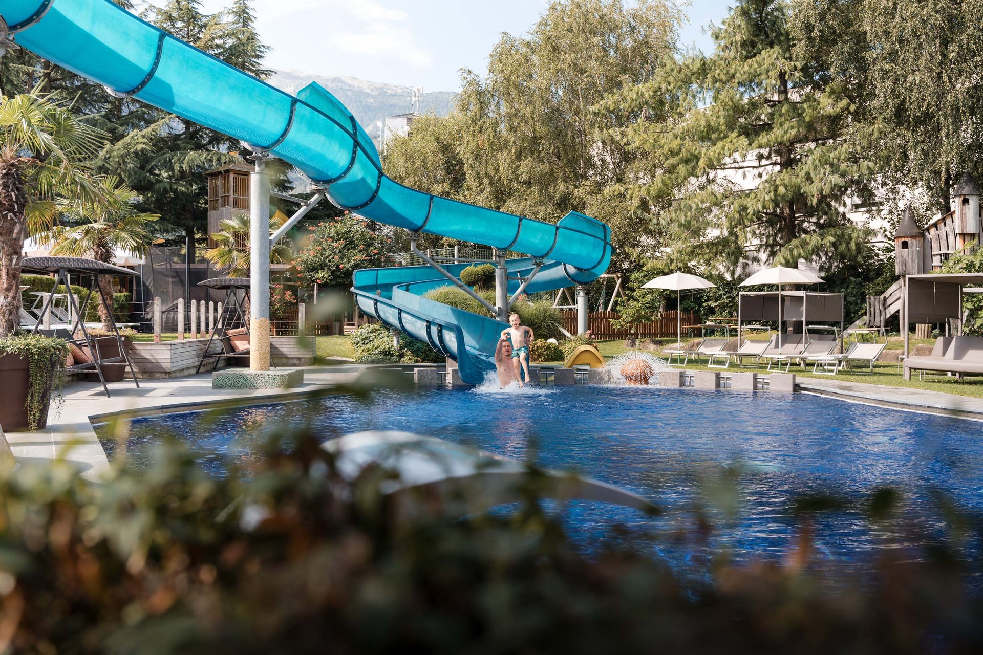 Euer fürstlicher Familienurlaub in Südtirol Vater und Kind springen ins Schwimmbecken von Wasserrutsche im Garten