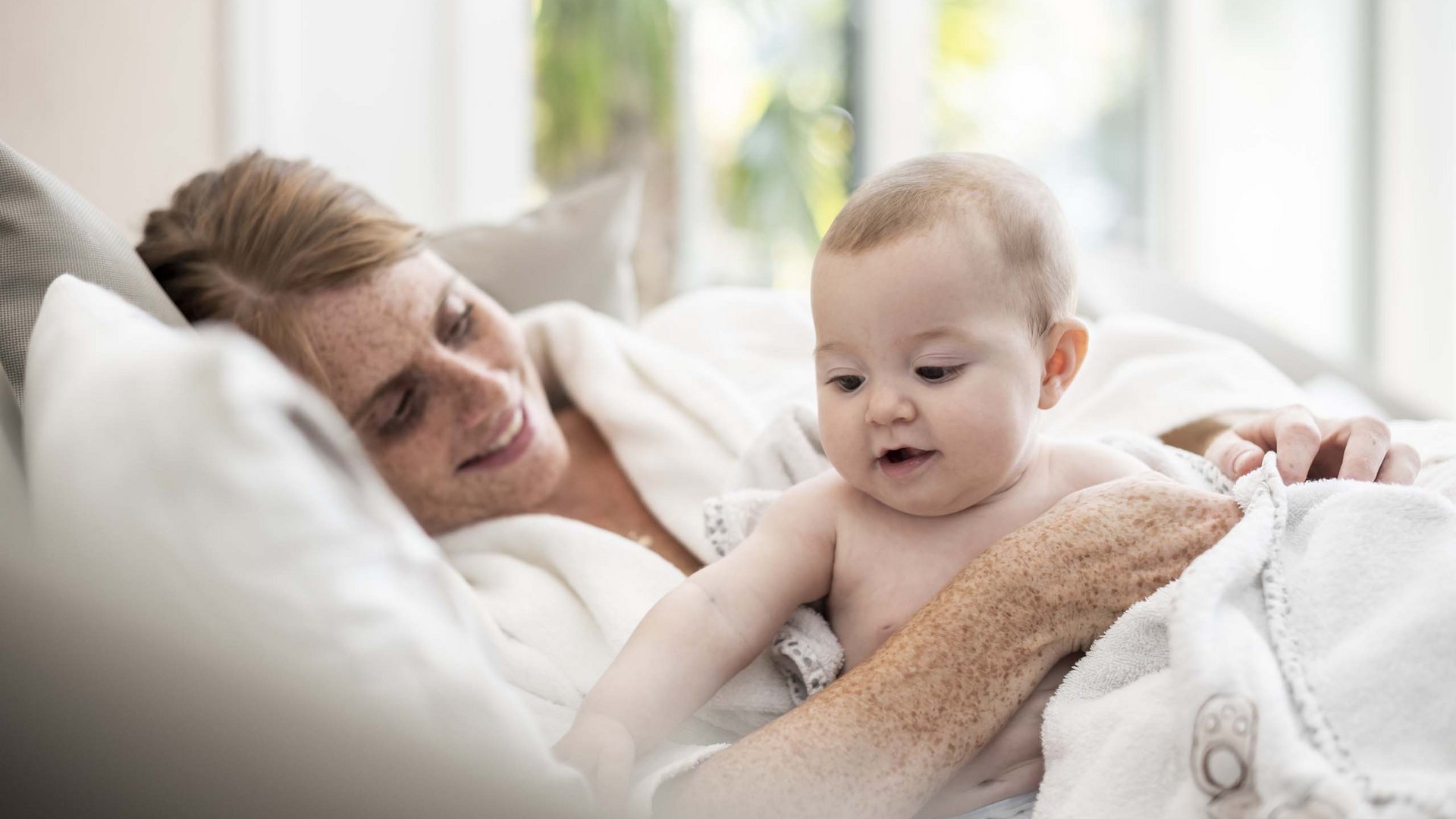 Euer Urlaub im Babyhotel in Südtirol Mutter lächelt und hält Baby, beide in weißen Decken eingewickelt