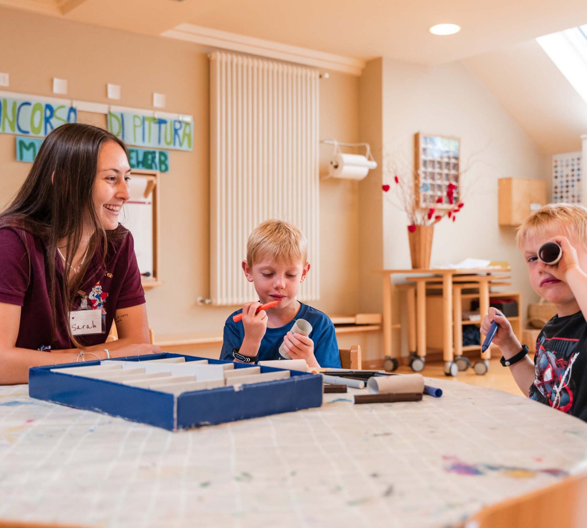 Spiel und Spaß im Hotel mit Kinderbetreuung in Südtirol Frau mit zwei Jungen beim Basteln an einem Tisch im Klassenzimmer