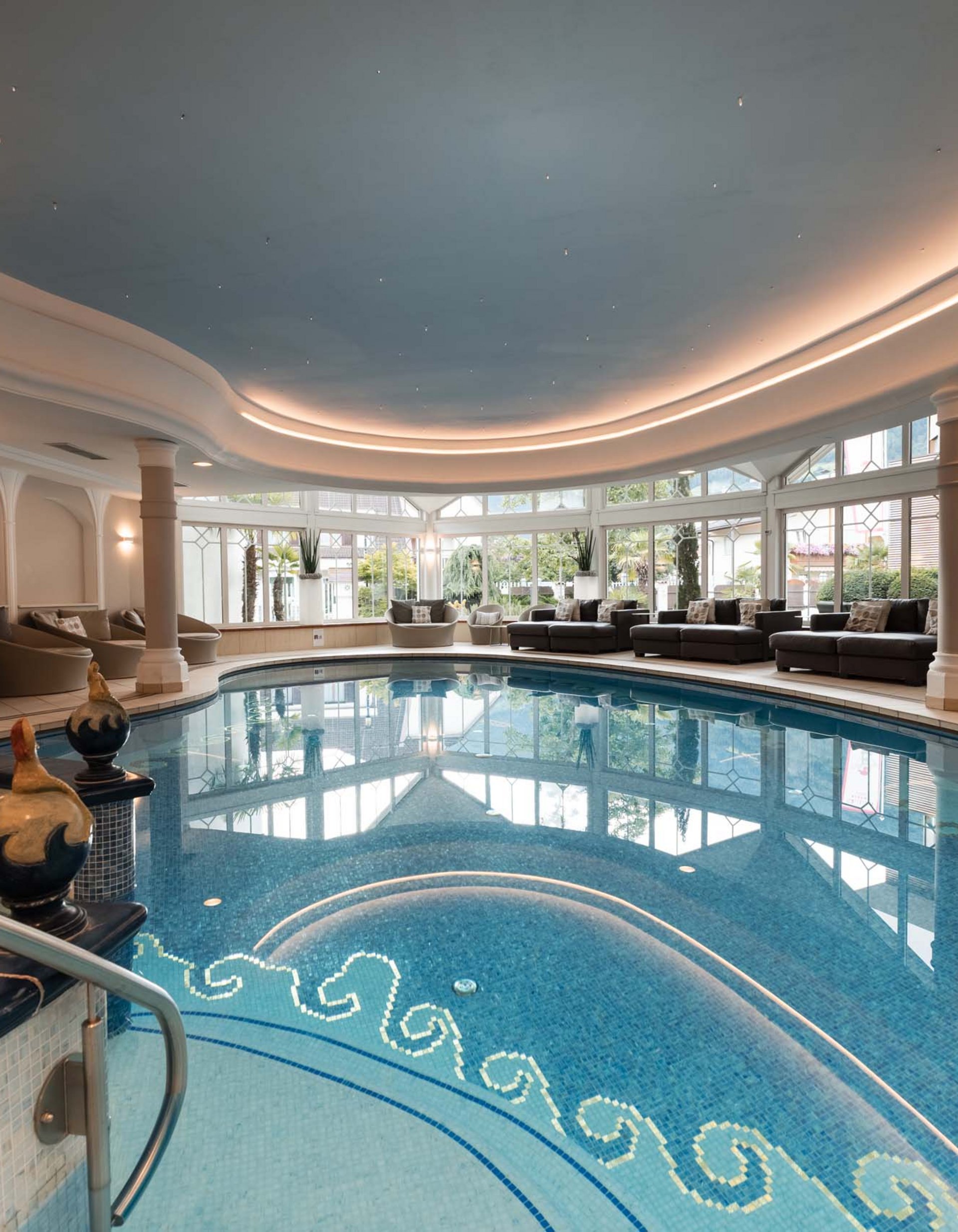 TYROL Family Retreat. Mehr als ein Familienhotel in Naturns. Eleganter Innenpool mit Sitzgelegenheiten und großen Fenstern