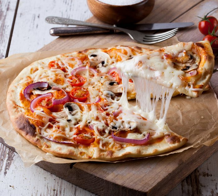Pure Flexibilität im TYROL Family Retreat Frische Pizza mit Käse, Tomaten, Pilzen und Zwiebeln auf Holzbrett