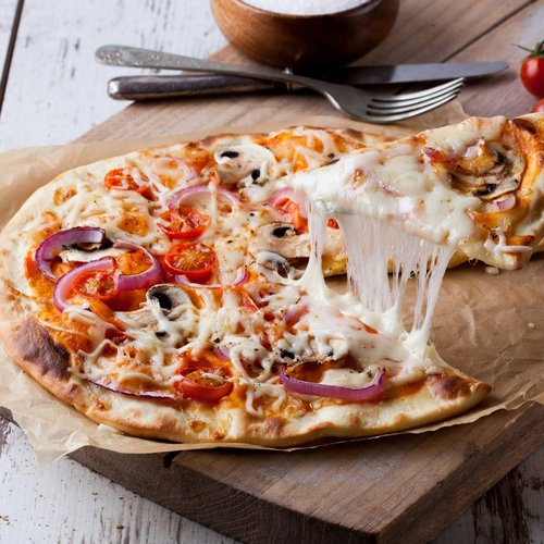 Pure Flexibilität im TYROL Family Retreat Frische Pizza mit Käse, Tomaten, Pilzen und Zwiebeln auf Holzbrett