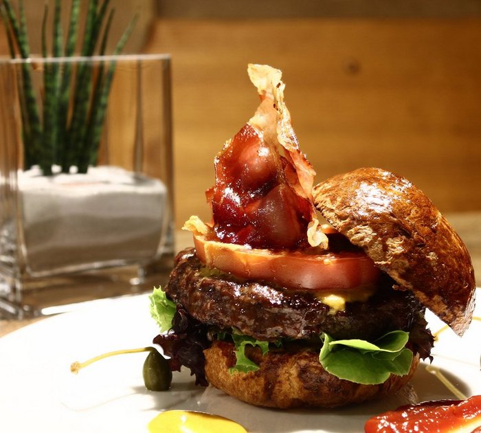 Pure Flexibilität im TYROL Family Retreat Hamburger mit Speck, Tomate, Salat und Soßen auf einem weißen Teller