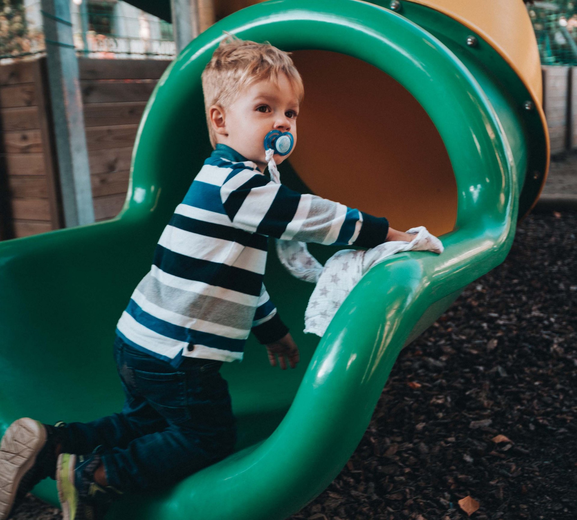 Euer Urlaub im Babyhotel in Südtirol Kleiner Junge mit Schnuller klettert auf grünem Spielplatzrutsch